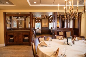 A dining area with wooden tables set for service, a bar area with a wine rack, and a view of the dining room in the background. - Plumsteadville Inn (Pipersville)