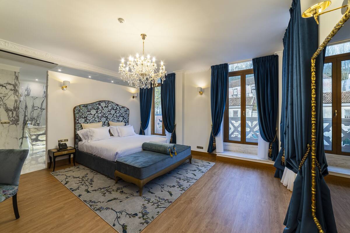 Un dormitorio amplio con una cama grande, un candelabro y vistas de la ciudad a través de ventanas panorámicas.