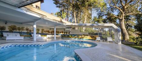 Una piscina con sillones de descanso y un patio techado.