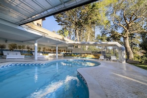 Una piscina con sillones de descanso y un patio techado.