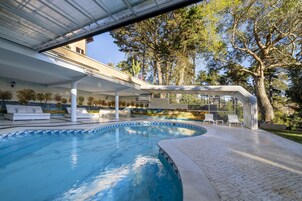 Una piscina con sillones de descanso y un patio techado.