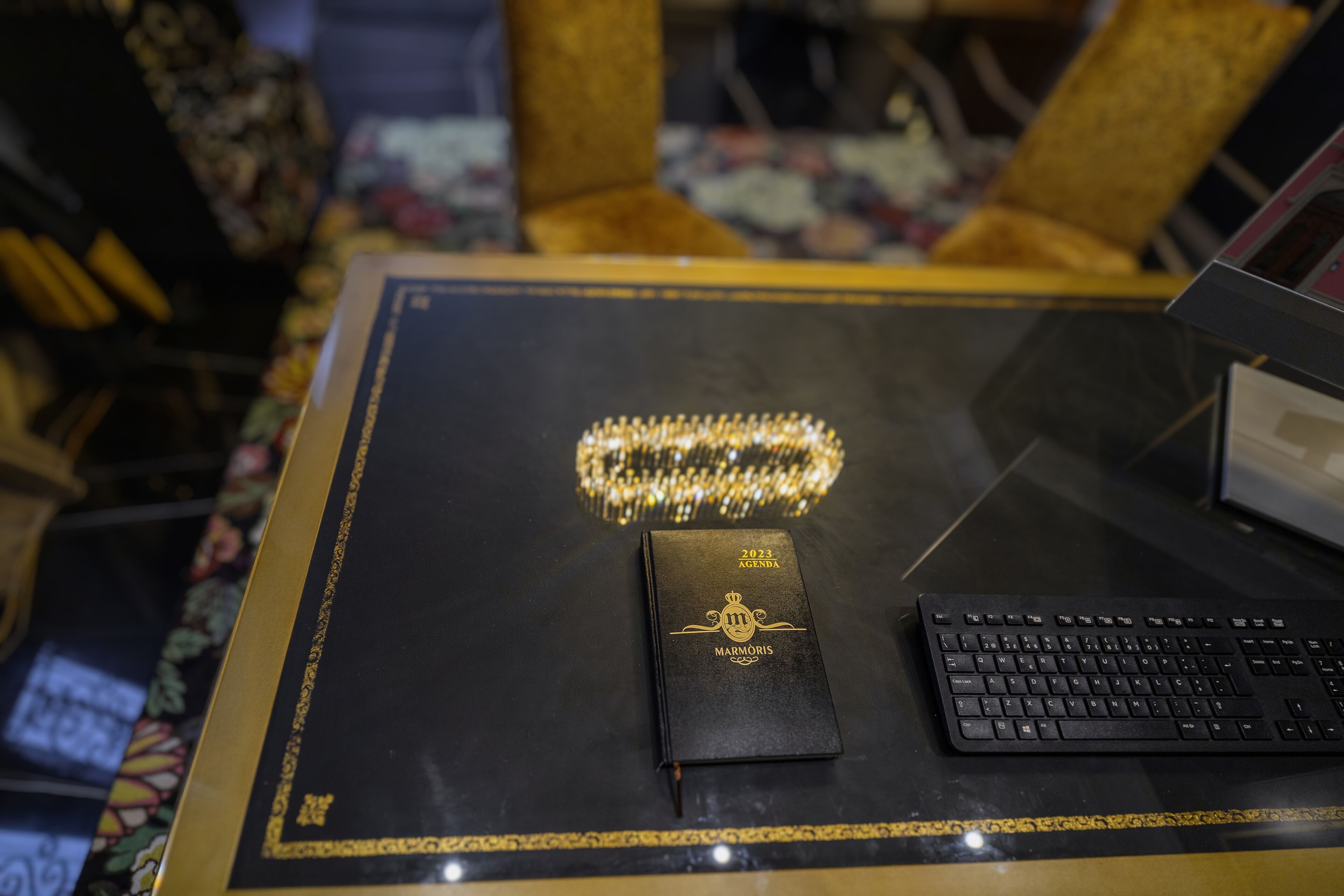 A black desk with a gold-framed notebook, a keyboard, and a decorative item.