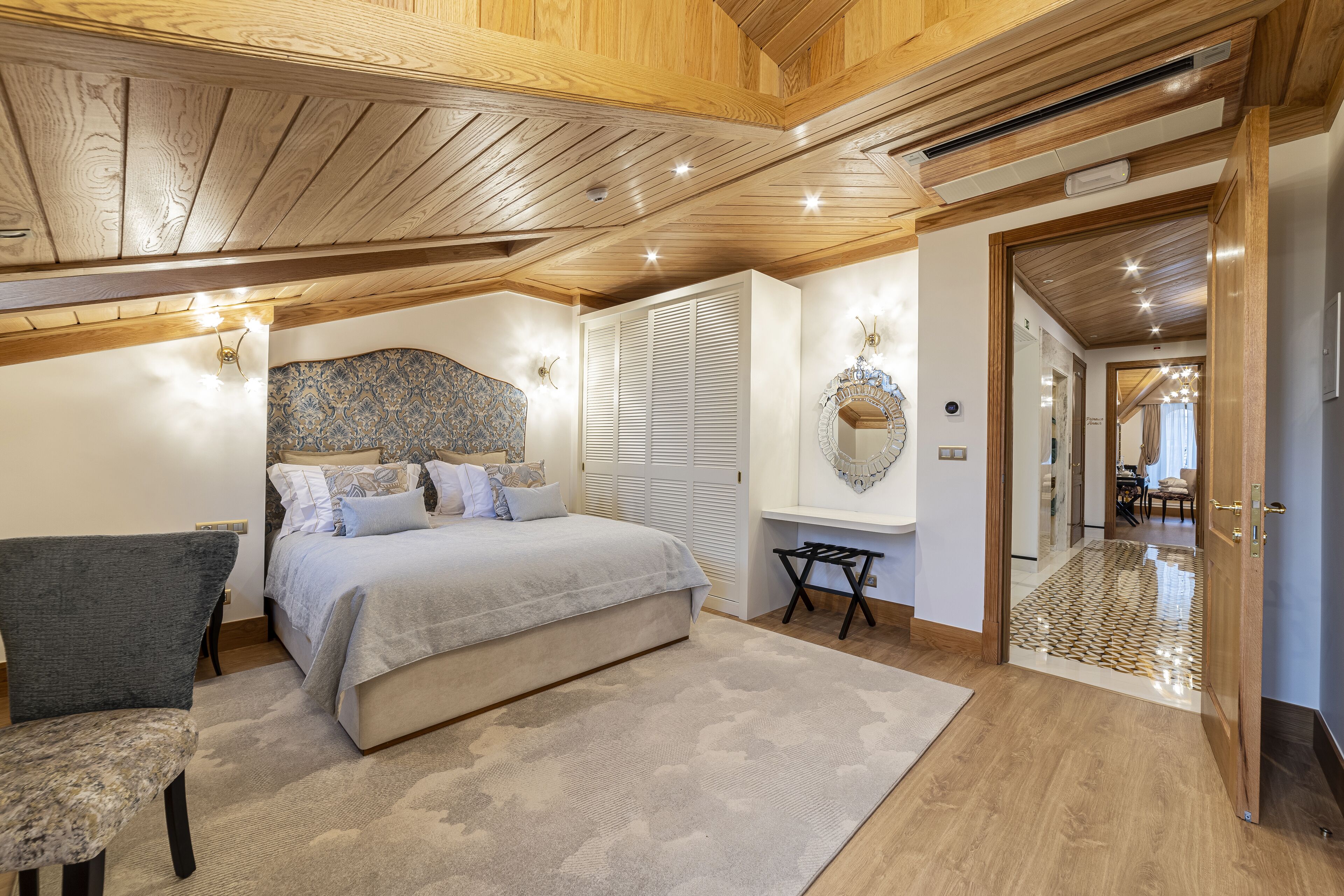A bedroom with a bed, a chair, a desk, and a mirror.