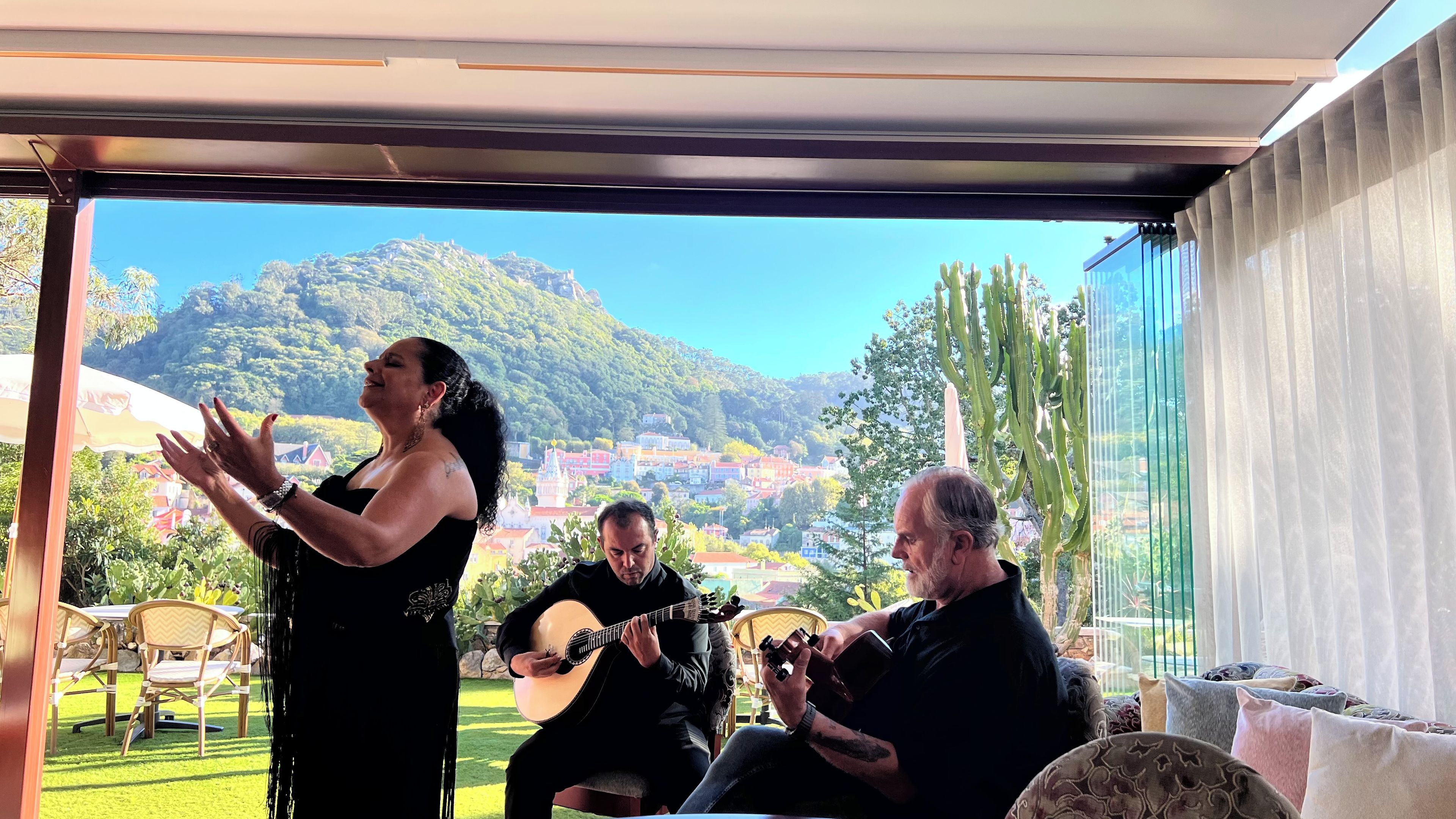 A room with a view of a mountainous landscape, a dining area with chairs, and a person playing a guitar.