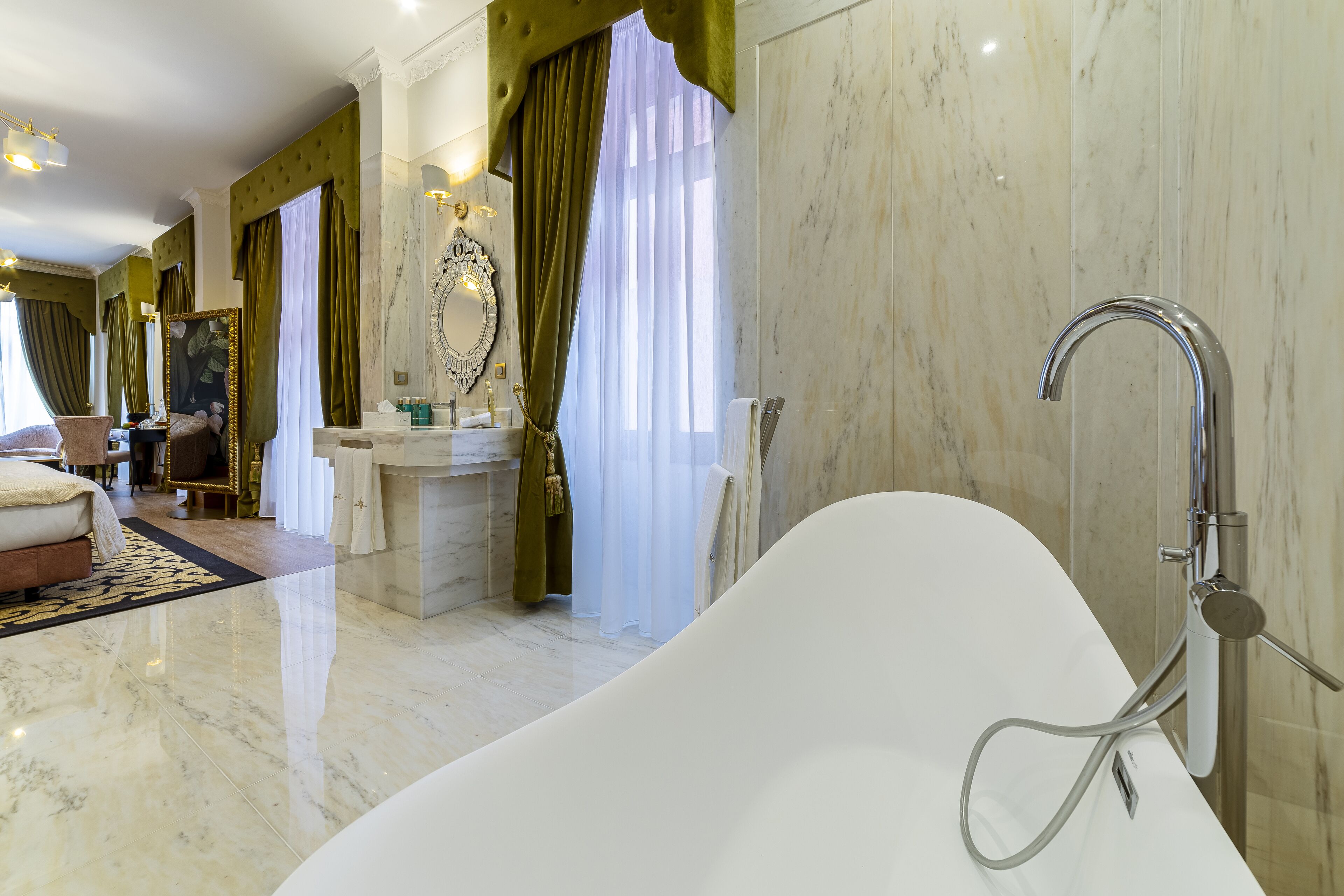 Un baño lujoso con una bañera independiente, suelo de mármol y un espejo grande con marco decorativo.