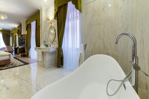 Un baño lujoso con una bañera independiente, suelo de mármol y un espejo grande con marco decorativo.