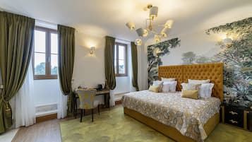 A bedroom with a large bed, a desk, and a chair. There are curtains on the windows, and a chandelier hangs from the ceiling.