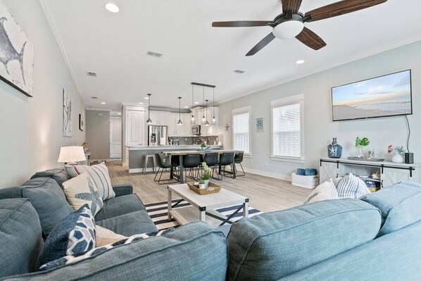 A modern living room with a gray sofa, a coffee table, and a dining area with a kitchen in the background.