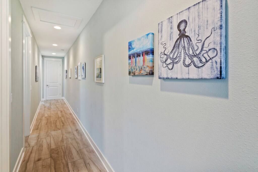 A hallway with wooden flooring, white walls, and several framed artworks including an octopus painting.