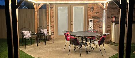 A covered patio with a table and chairs, a brick wall, and a wooden roof structure.