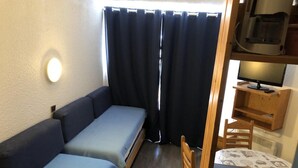 Een compacte kamer met een slaapbank, een klein tafeltje en een stoel.