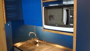 Een kleine keuken met een roestvrijstalen spoelbak, een magnetron en een klein fornuis.