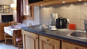 Een kleine keuken met houten kastjes, een magnetron, een koffiezetapparaat en een spoelbak.