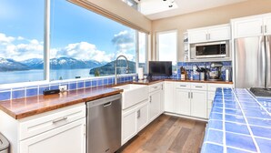 Una cocina moderna con armarios blancos, una encimera de madera y vistas a montañas y un lago.