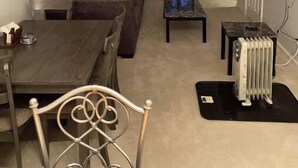 A living room with a dark brown sofa, a coffee table, and a dining table with chairs. There is a radiator on the floor and a television mounted on the wall. - Sunny Spitz Den (Basye)