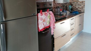 Una cuina moderna amb un frigorífic d'acer inoxidable, forn integrat i microones. Hi ha armaris de fusta i una façana de rajola.