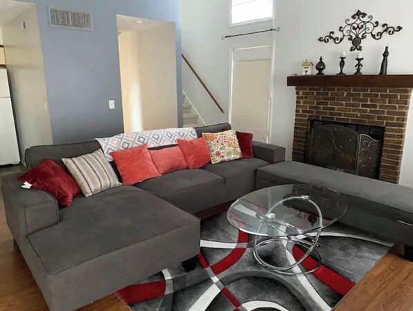 A living room with a grey sectional sofa, a glass coffee table, and a red and grey patterned rug.