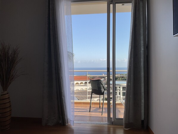 A room with a sliding glass door leading to a balcony with a view of the ocean.