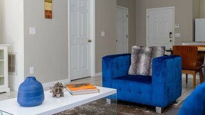 A living room with a blue sofa, a white coffee table, and a book. There are two white doors and a small painting on the wall. - Cozy 3 bedroom home with Private Pool 4564 (Kissimmee)