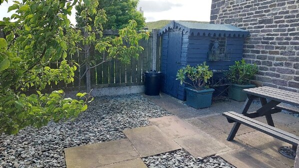 A patio area with a stone floor, a wooden bench, and potted plants.