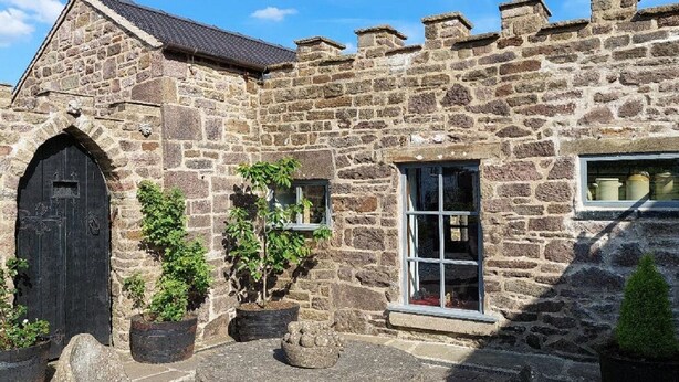 Un edificio de piedra con un gran arco de entrada, una ventana y macetas con plantas.