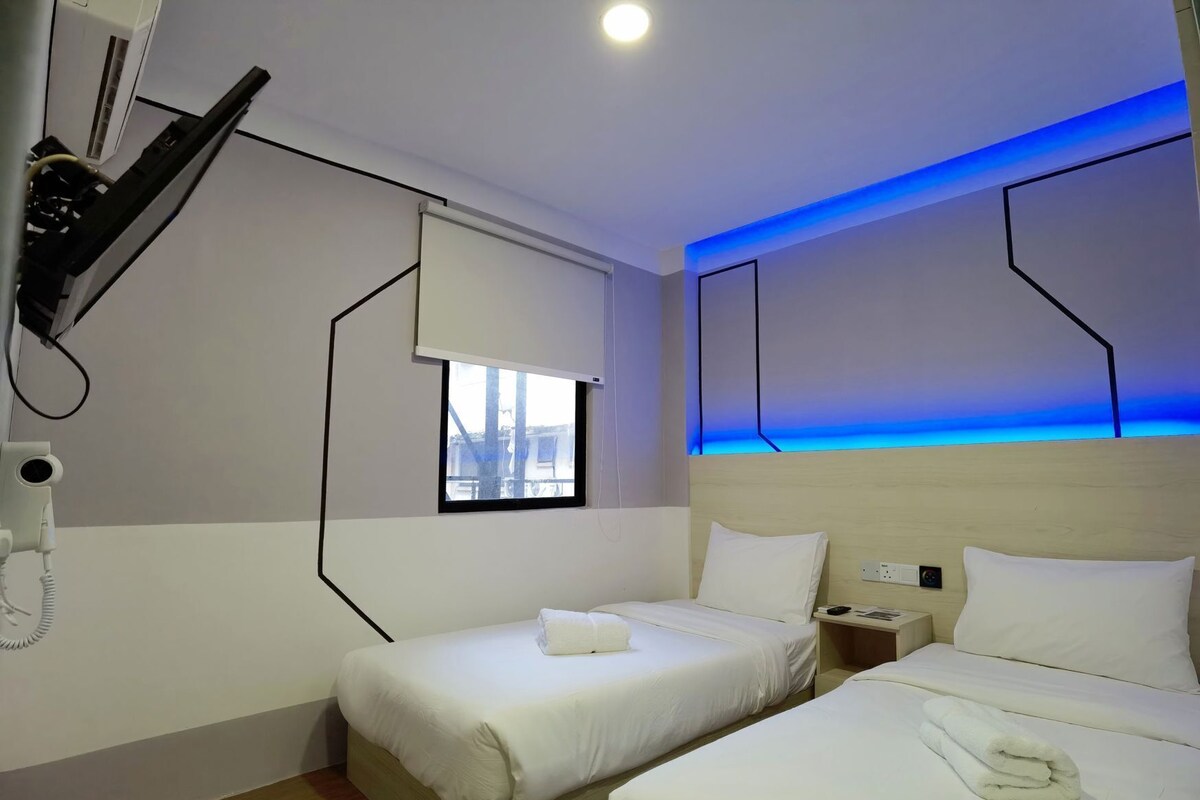 A hotel room with two beds, a window, a phone, and a wall-mounted heater.
