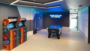 Un espacio interior moderno con máquinas de videojuegos, mesa de billar y un letrero de neón.