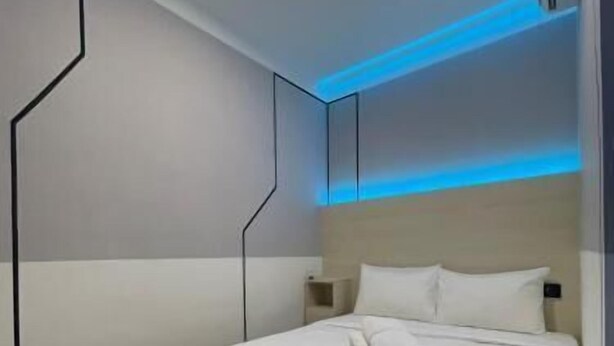 Una habitación de hotel moderna con una cama bien hecha, una mesita de noche y una pared con lámparas geométricas.