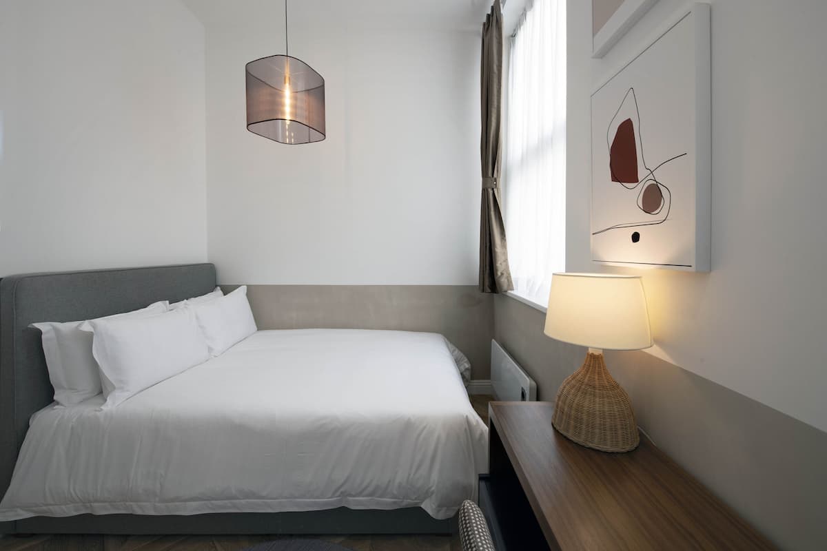A neatly made bed with white linens, a bedside lamp, and a wall-mounted abstract art piece.