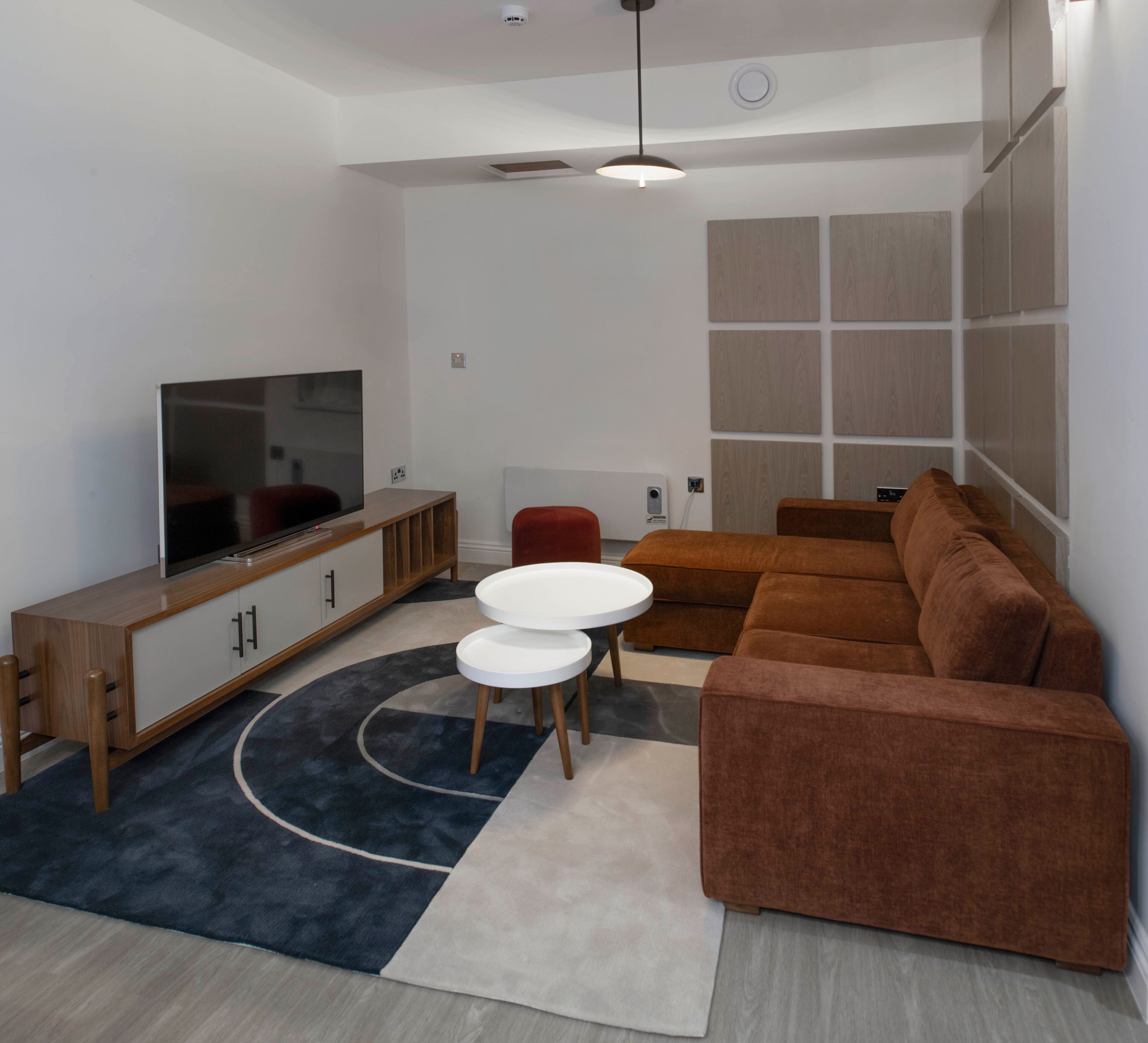 Una sala de estar moderna con una televisión de pantalla plana, un mueble de madera, un sofá marrón, un sillón rojo y una mesa de centro blanca.
