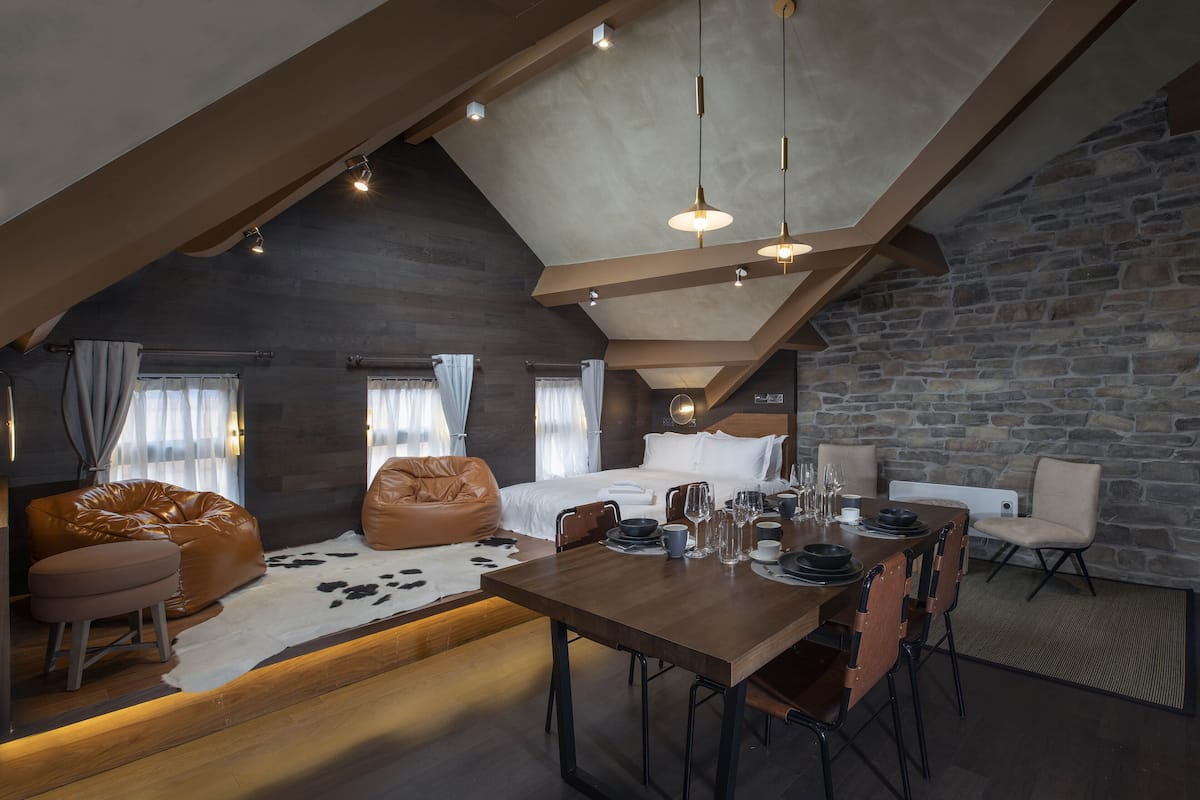 A modern loft bedroom with a sloped ceiling, exposed beams, and a stone wall.