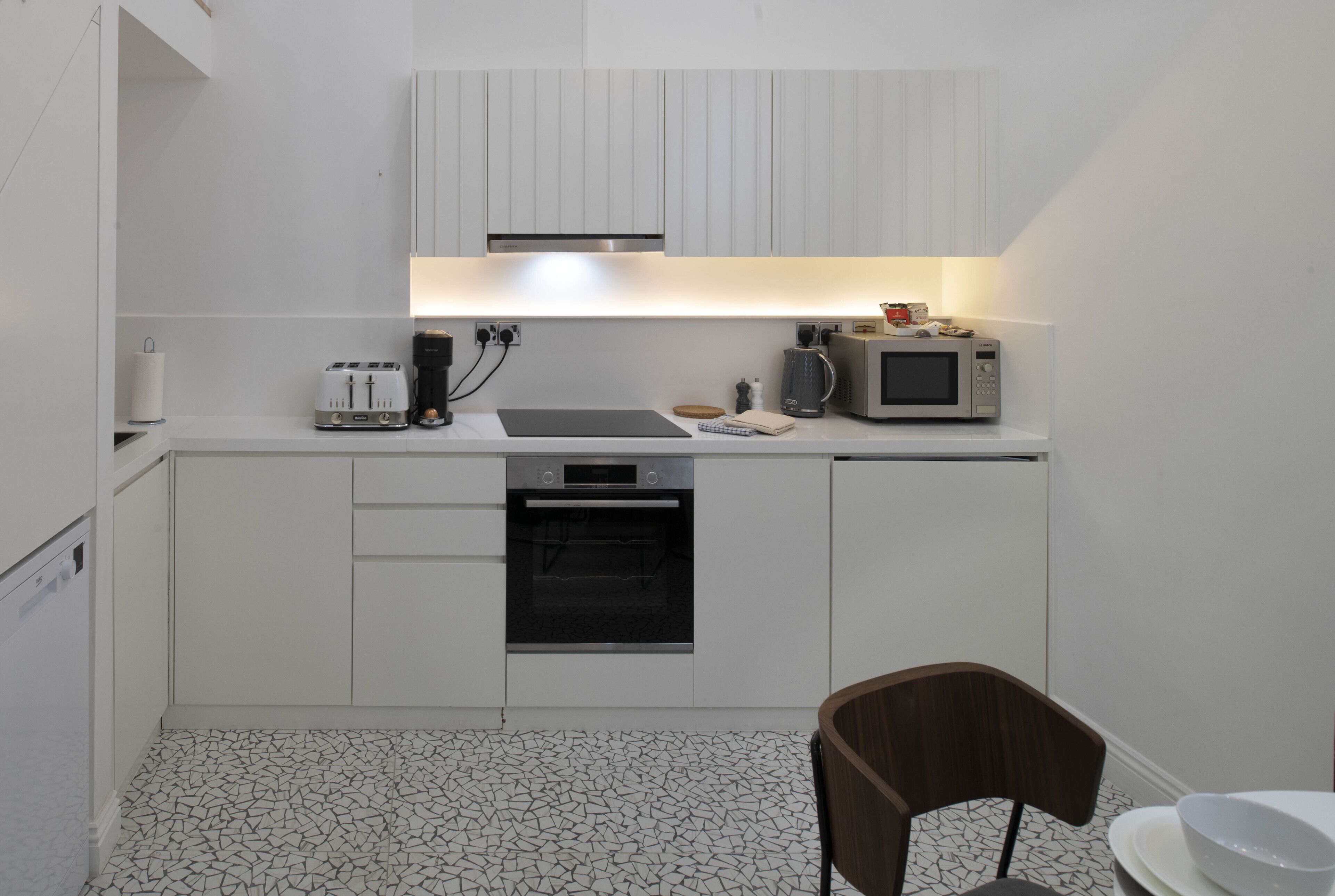 Une cuisine compacte avec des meubles blancs, un four à micro-ondes, un grille-pain et une machine à café.