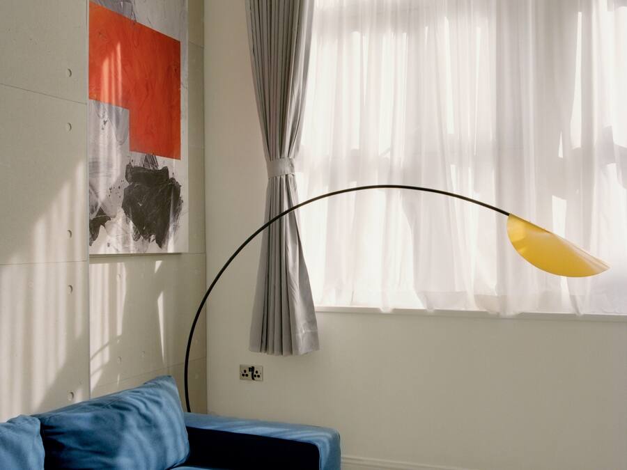 A modern living room with a blue sofa, a painting on the wall, and a window with sheer curtains.