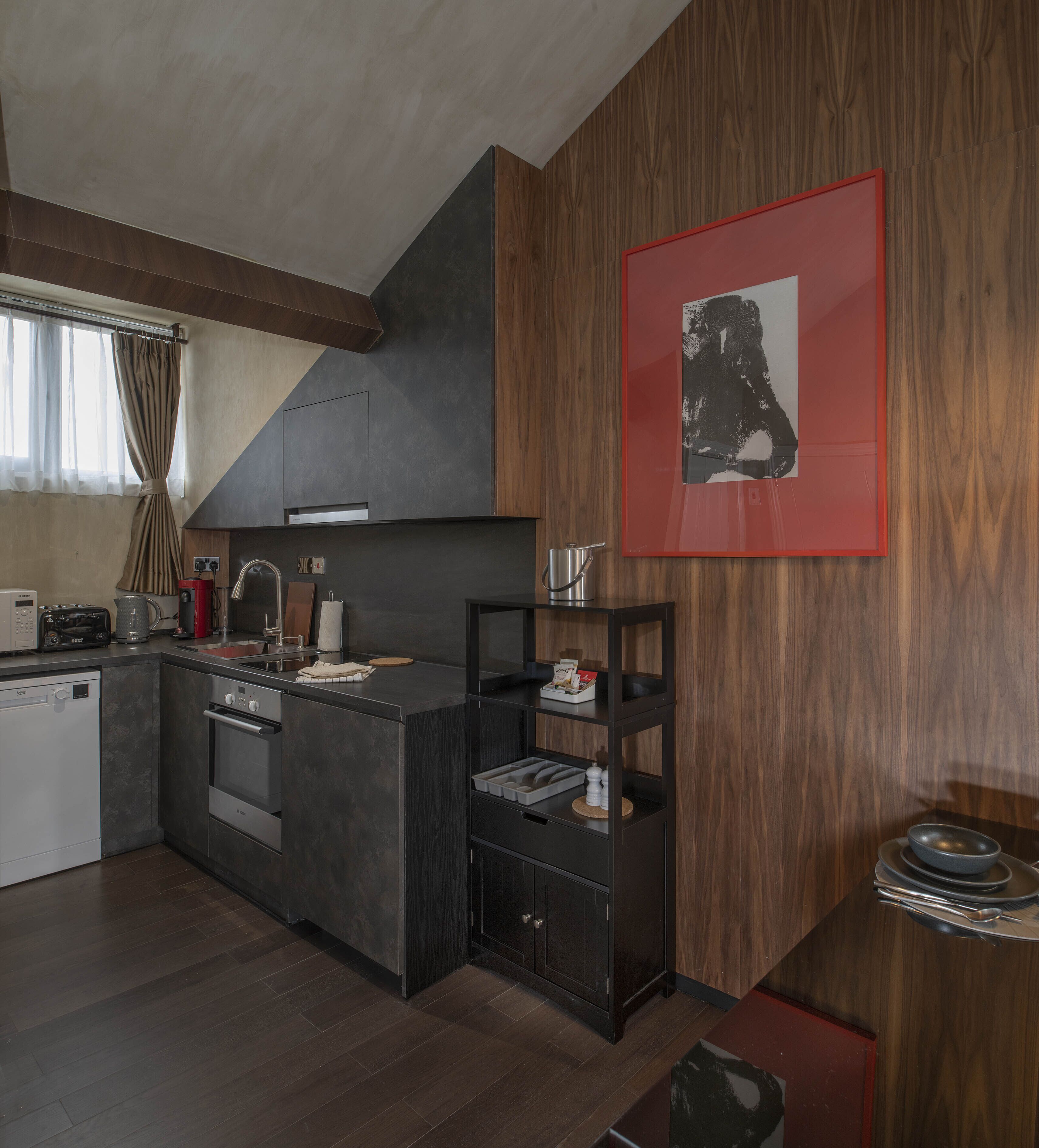 A modern kitchen with dark cabinetry, a built-in oven, and a microwave. There is a wooden wall panel and a framed artwork above the counter.
