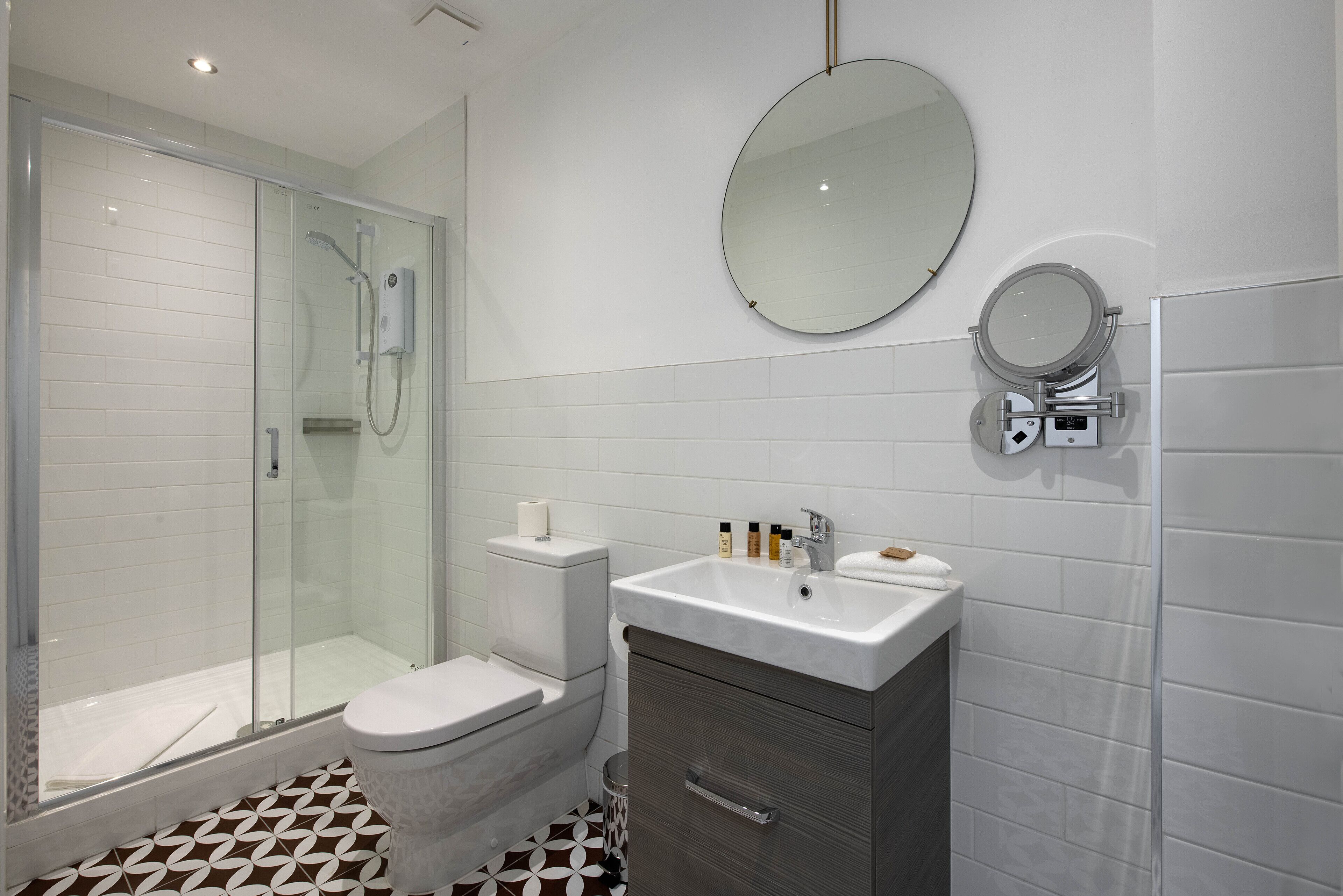 A modern bathroom with a glass-enclosed shower, a toilet, a sink with toiletries, and a mirror.