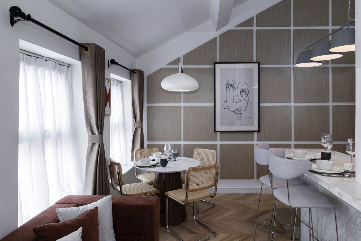 A modern hotel room with a brown sofa, a dining table with chairs, and a bar area.
