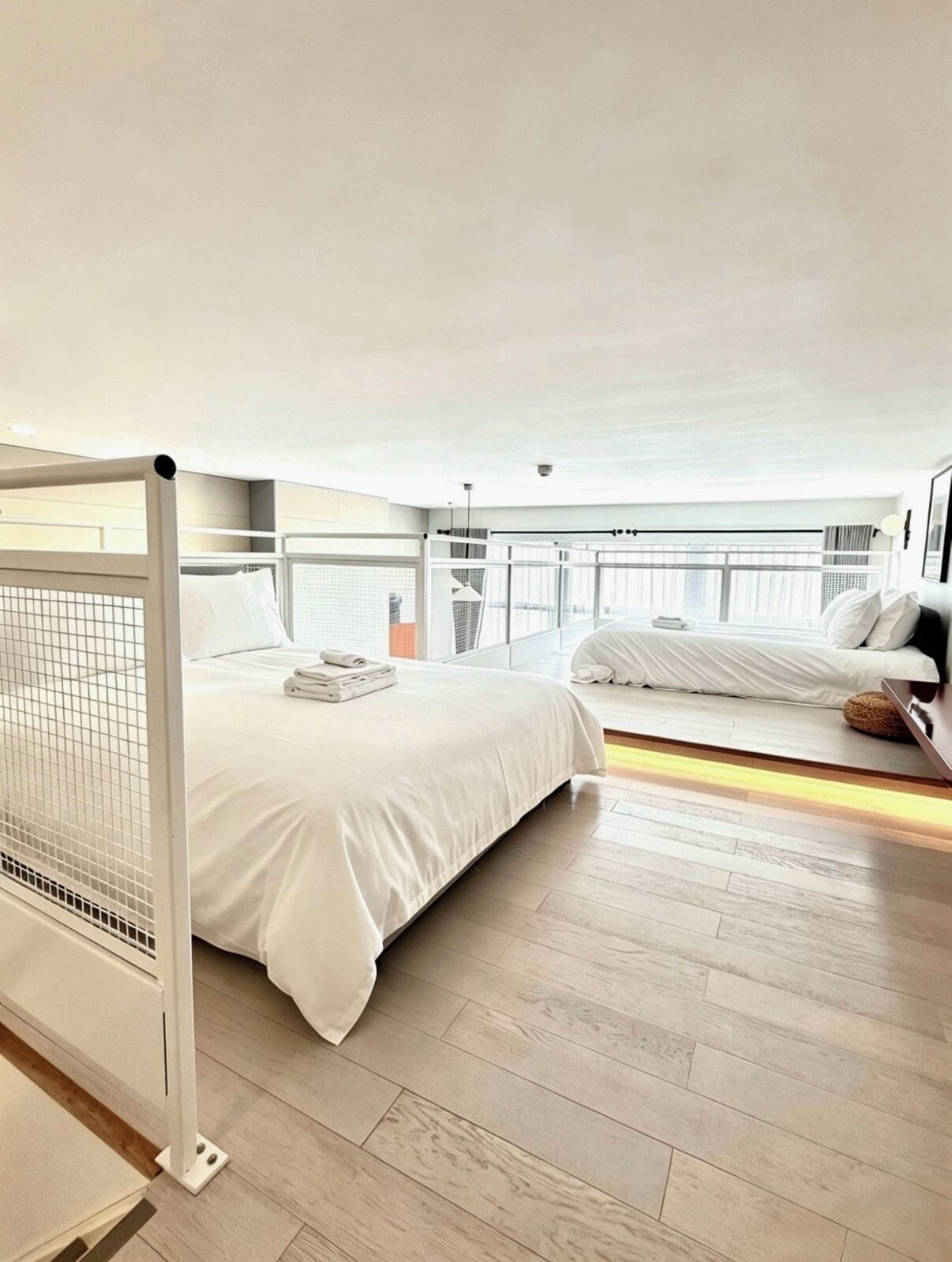 A modern hotel room with a large bed, a smaller bed, a balcony, and a view of the city.