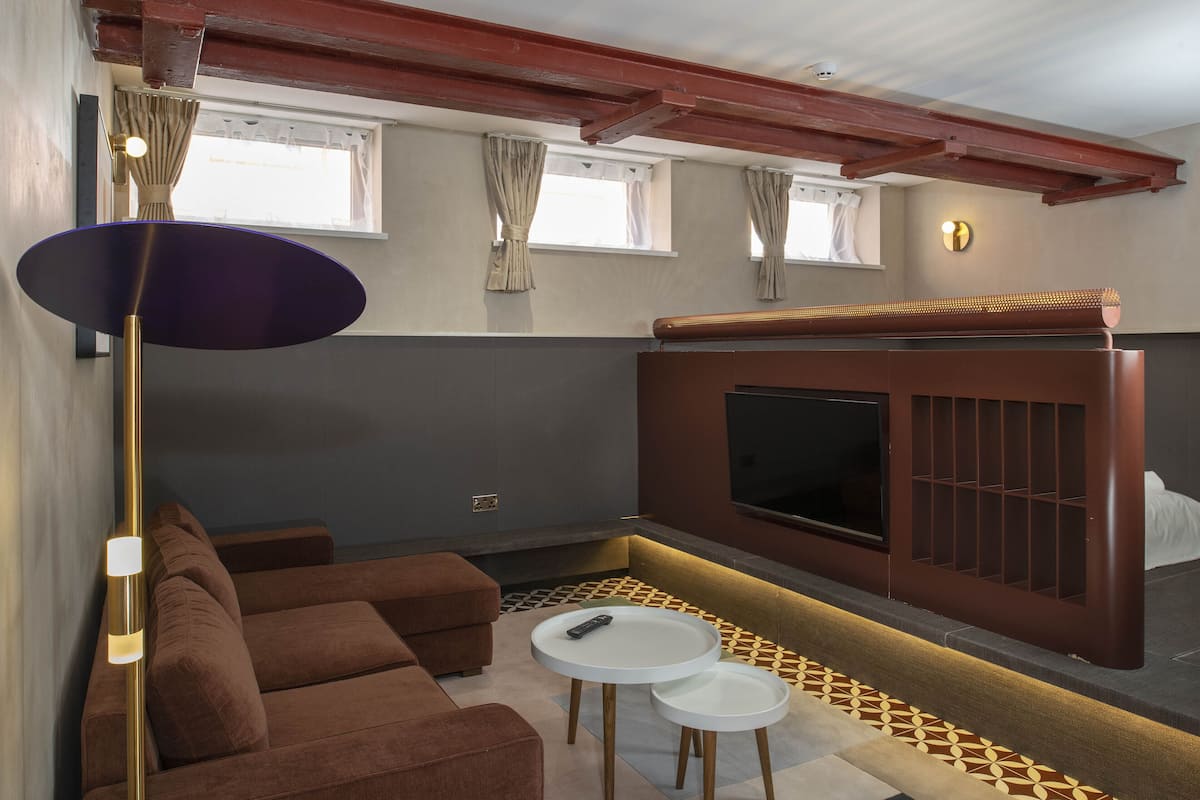 A modern living room with a sofa, two small tables, a TV mounted on a wall, and a patterned floor.