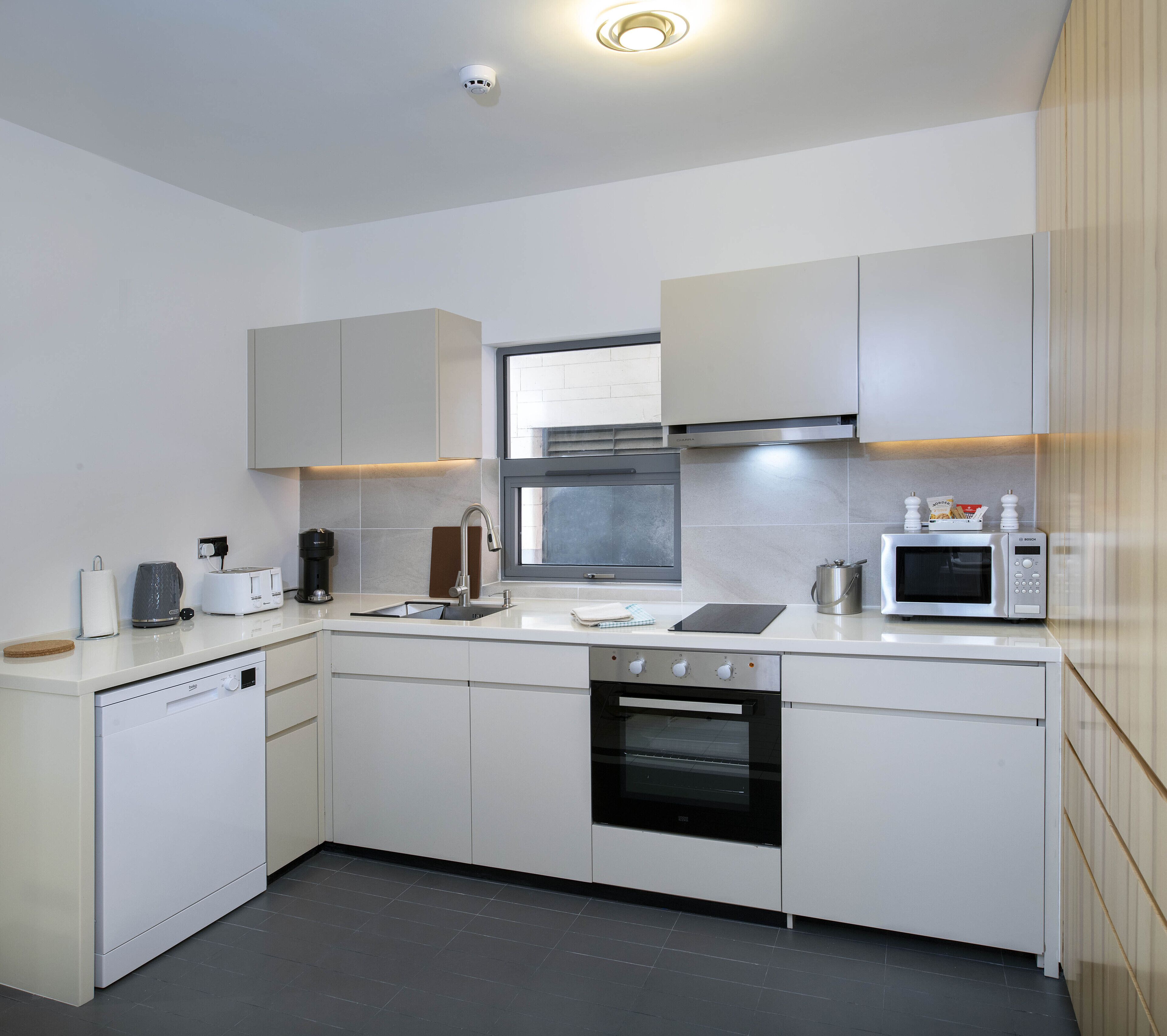 A modern kitchen with white cabinetry, a built-in oven, a microwave, and a dishwasher.