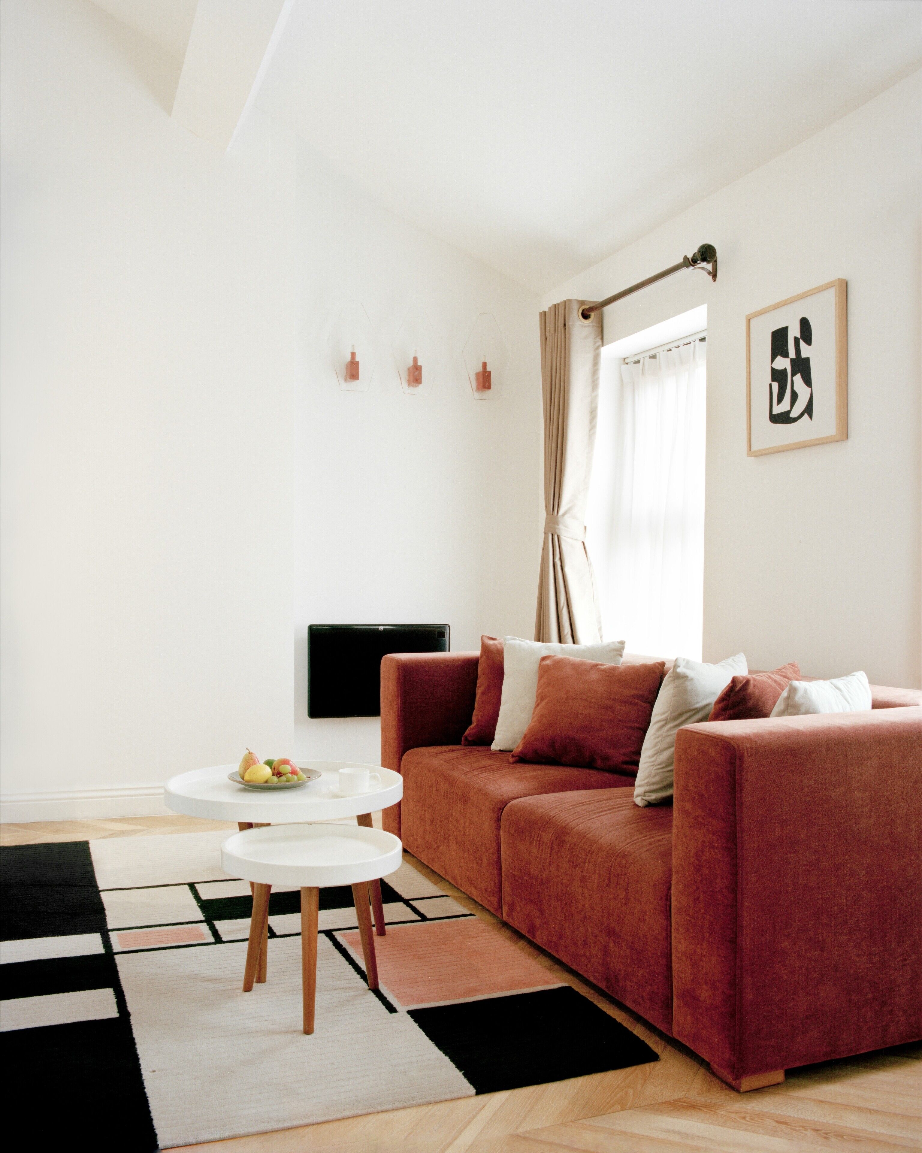 A modern living room with a red sofa, two white side tables, a flat-screen TV, and a fruit bowl on one of the tables.