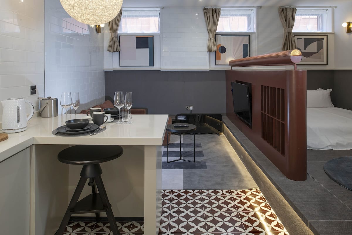 A compact hotel room with a kitchenette, a dining area, a bed, and a TV.
