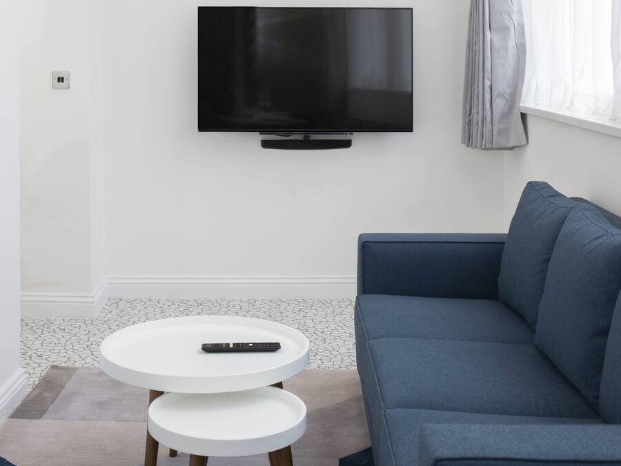 A modern living room with a flat-screen TV mounted on the wall, a blue sofa, and a white round coffee table with a remote control on it.