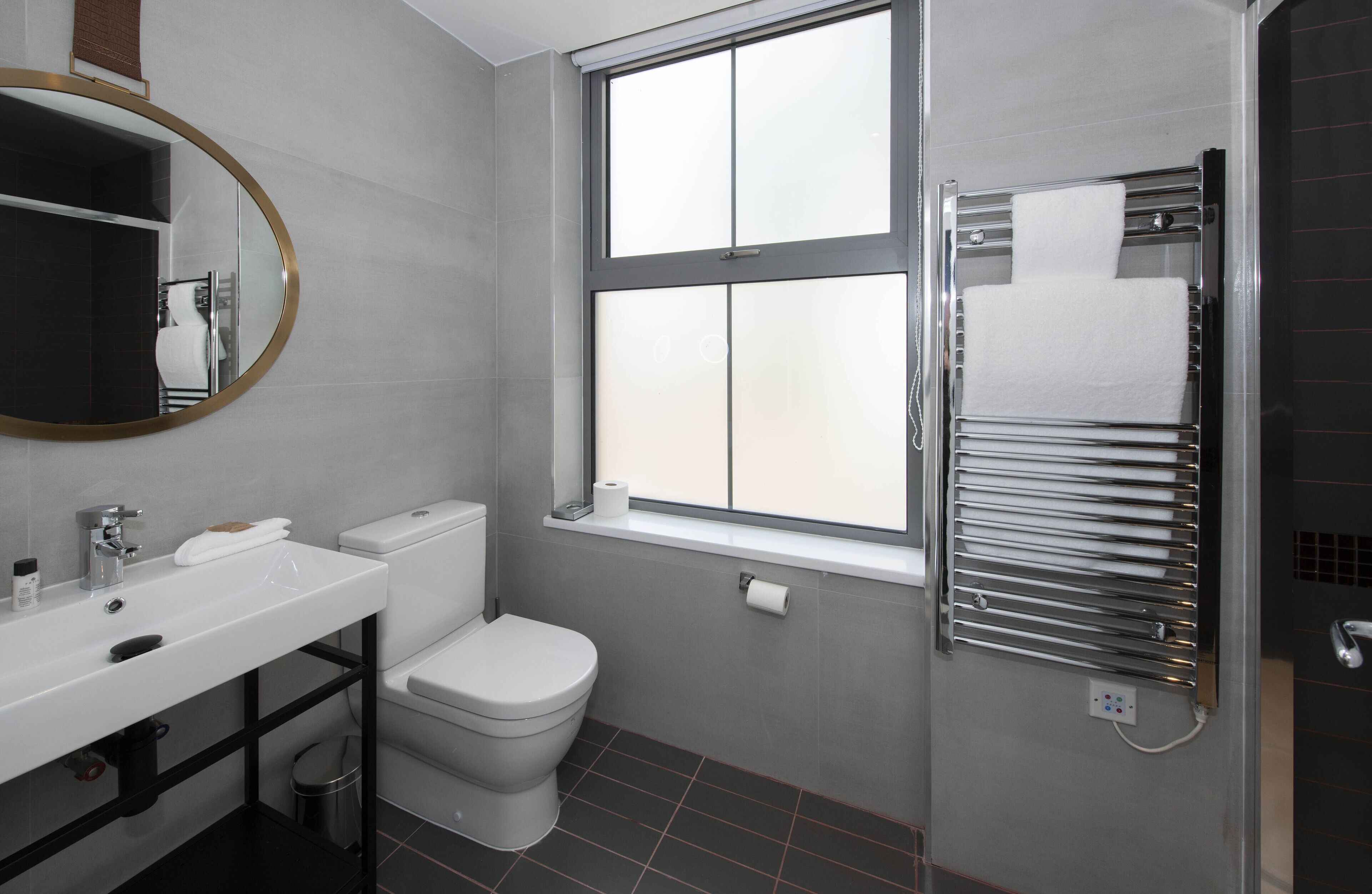 A modern bathroom with a white sink, toilet, and a window above the shower.