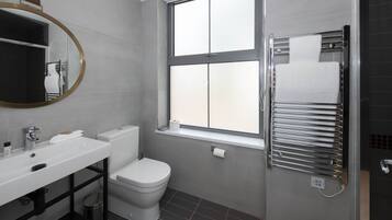 A modern bathroom with a white sink, toilet, and a window above the shower.