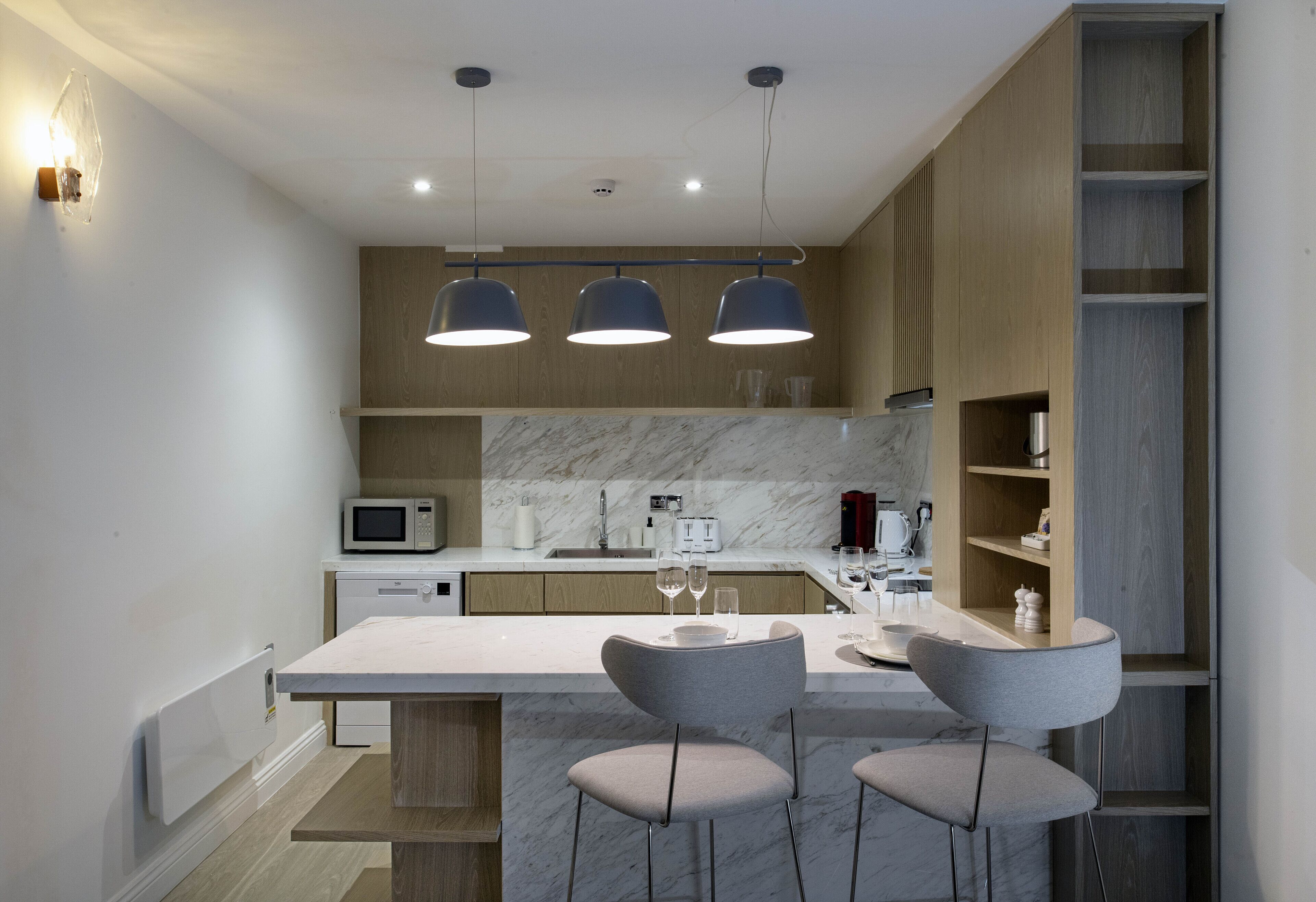 A modern kitchen with a marble countertop, three pendant lights, and a built-in microwave.