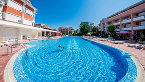 A swimming pool with a person swimming, surrounded by lounge chairs and umbrellas, with buildings in the background. - Studio - Sleeps 4 & Access to Pools (Sunny Beach)