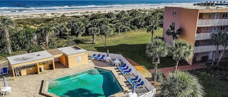 Zona de piscina amb gandules, una petita piscina i vista a la platja i l'oceà.