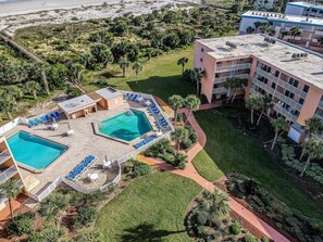 A resort with a swimming pool, lounge chairs, and a building with balconies. - SunLounger|3BR/2BA Beachfront Retreat (Saint Augustine Beach)