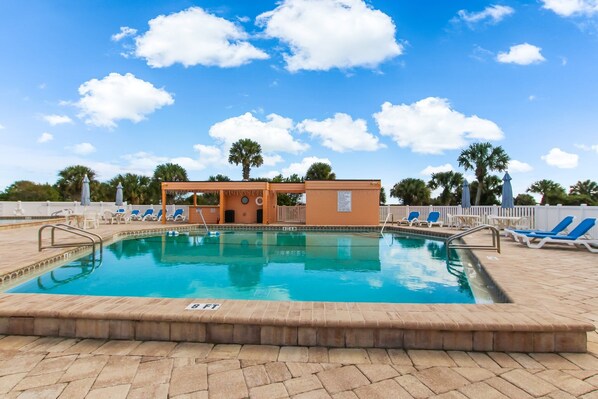 A swimming pool with lounge chairs, a small building, and palm trees in the background.