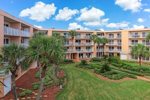 A multi-story hotel with balconies, a landscaped garden, and a clear blue sky.